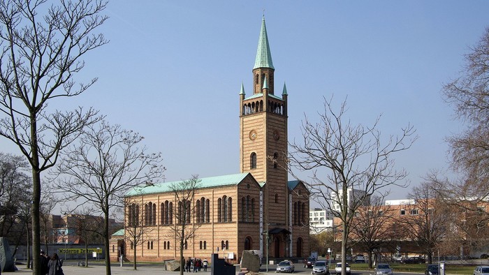 Große Kirche mit hohem Turm und grünem Dach in einem Park mit Bäumen und Menschen