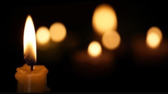 Ein einzelnes brennendes Kerzenlicht vor unscharfem Hintergrund, begleitet von Text in deutscher Sprache.