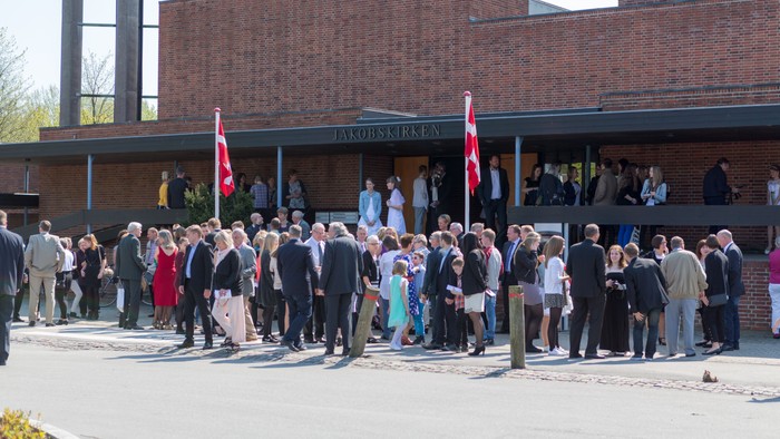 En gruppe af mennesker står foran et rødt murstensbygning med flag.