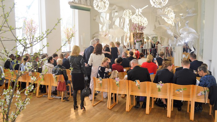 En gruppe af mennesker sidder ved bord i et lys og moderne rum med kunst på væggen.