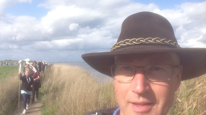 En mand med hat og briller går på en sti gennem en naturpark.