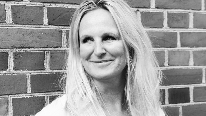 En kvinde med blond hår står foran en mur af ruder.