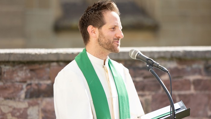 Mann in weißem Hemd und grüner Schärpe spricht in Mikrofon