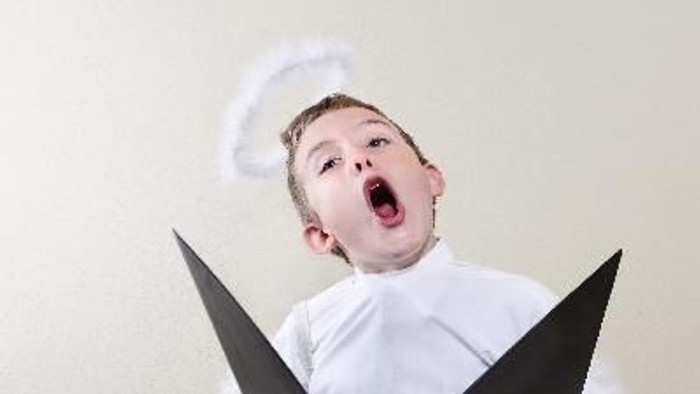 Ein Mann im Engelkostüm hält ein aufgeschlagenes Buch und schreit.