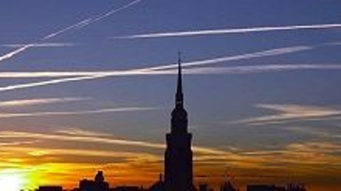 Ein hoher Turm vor einem Himmel mit Sonnenuntergang und Kondensstreifen.
