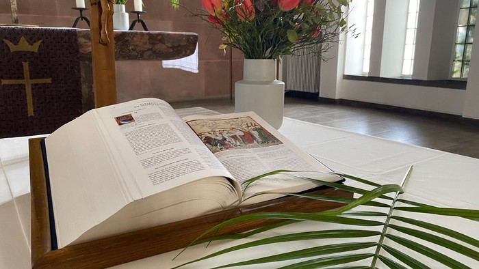 Offene Bibel auf Altar mit Blumen und Palmenwedel