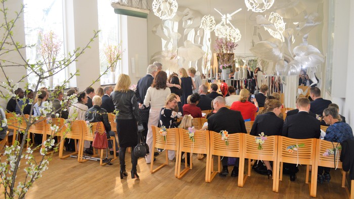 En gruppe af mennesker sidder ved bord i et lys og moderne rum med kunst på væggen.