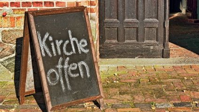 Das Schild steht vor einer Holztür und zeigt "Kirche offen" an.