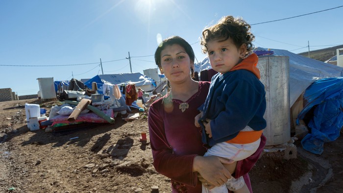Eine Frau hält ein Kind in einem Lager, umgeben von Zelten und Habseligkeiten.