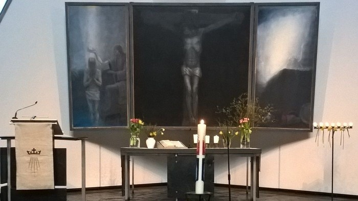 Gedenkkapellenbühne mit brennenden Kerzen, Blumengestecken und einem zentralen Kerzenständer.