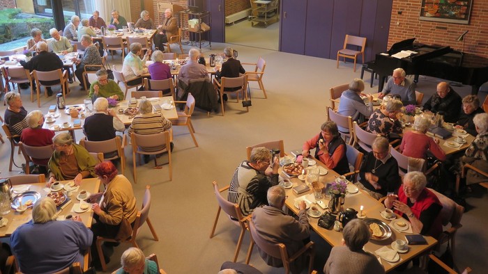 En gruppe ældre folk spiser sammen i en stor hall.