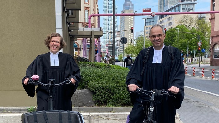 Zwei Personen in Roben fahren Fahrräder durch die Stadt.