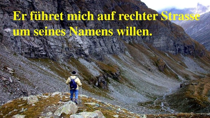 Ein einsamer Wanderer steht auf einem felsigen Bergpfad mit einer malerischen Bergkulisse und deutschem Text im Vordergrund.