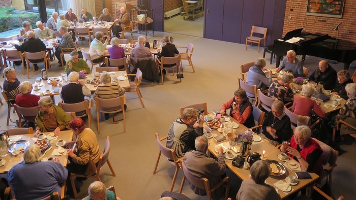 En gruppe ældre folk spiser sammen i en stor hall.