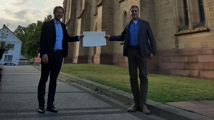 Zwei Männer halten Schild vor Kirche.