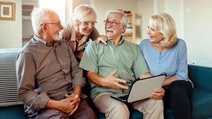 Eine Gruppe älterer Freunde sitzt gemütlich auf einem Sofa und unterhält sich.