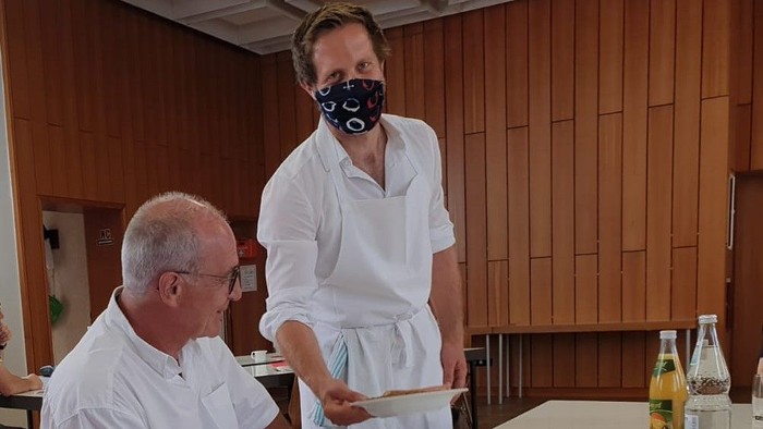 Ein Mann und eine Frau in Schürzen stehen an einem Tisch, die Frau hält ein Tablett.