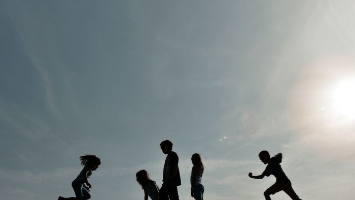 Silhouetten von Kindern springen und spielen auf Felsen unter klarem Himmel