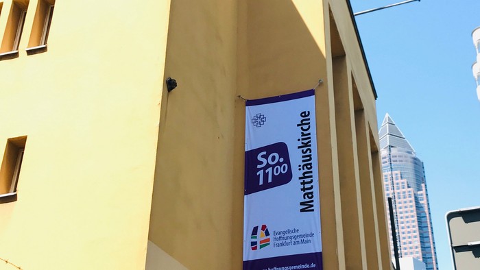 Gelbe Gebäudeecke mit Werbung für Mathematikwoche und Skyline im Hintergrund