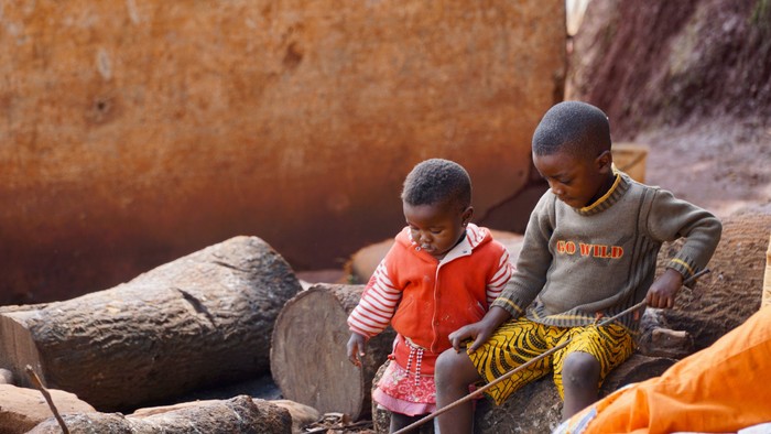 Zwei Kinder sitzen vor einer Lehmhütte und spielen.