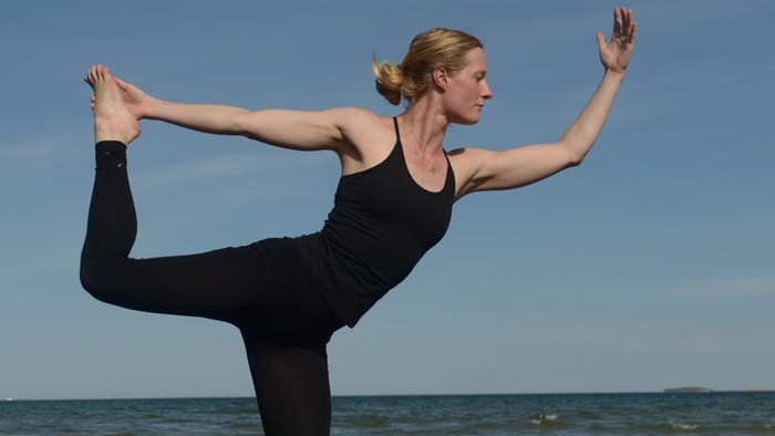 En kvinde udfører yoga ved stranden.