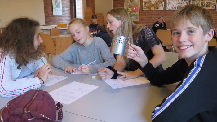 En gruppe af elever sidder om en bord i en klassesal og arbejder med papirer.