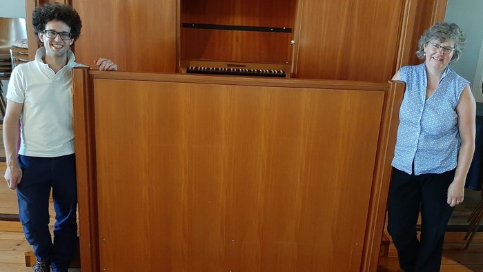 Zwei Personen stehen neben einem hölzernen Klavier.