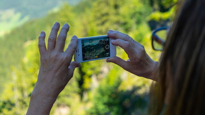 Eine Person hält ein Smartphone und macht ein Foto von einer grünen Landschaft.