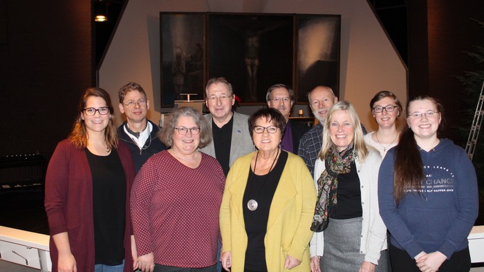 Gruppe von Personen, die drinnen gemeinsam posieren, mit einem modernen architektonischen Hintergrund und warmer Beleuchtung.