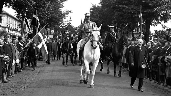 En riddende hest med rytter i en parade forbi en folkemængde.