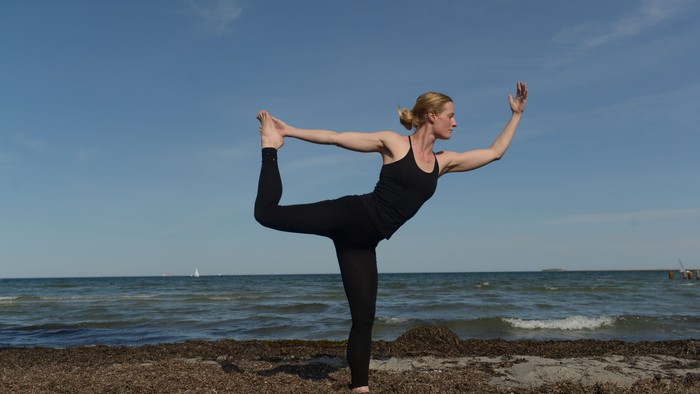 En kvinde udfører yoga på en klippe ved stranden.