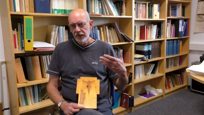 Ein älterer Mann hält ein gelbes Blatt Papier in einer Bibliothek.