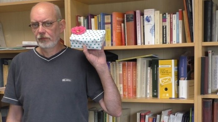 Mann hält ein kleines Geschenk vor Bücherregalen