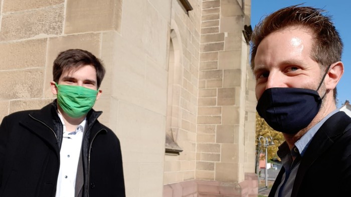 Zwei Männer mit Mund-Nasen-Schutz vor Steinmauer