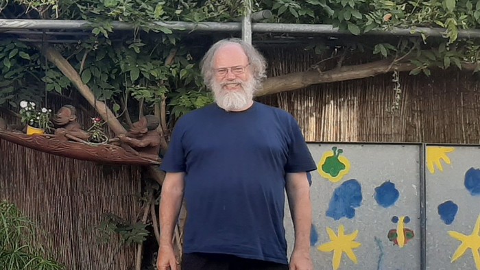 Mann mit weißem Bart vor bemaltem Holzzaun