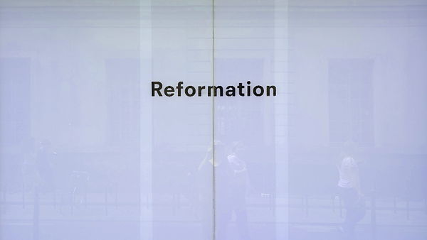 Schaufenster aus Milchglas mit dem Wort 'Reformation'. Passanten spiegeln sich darin.