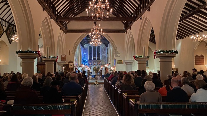 Church interior with congregation seated in pews, chandeliers hanging from high ceiling.