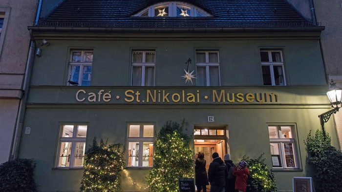 Vor dem Café St. Nikolai Museum stehen zwei Weihnachtsbäume und Menschen vor dem Gebäude.