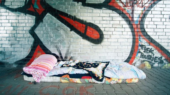 Ein Obdachloser schläft auf einer Decke vor einem Graffiti-Wand.