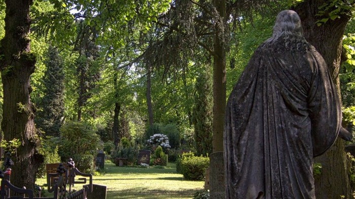 Eine friedvolle Friedhofstatue, umgeben von üppigem Grün und hohen Bäumen.