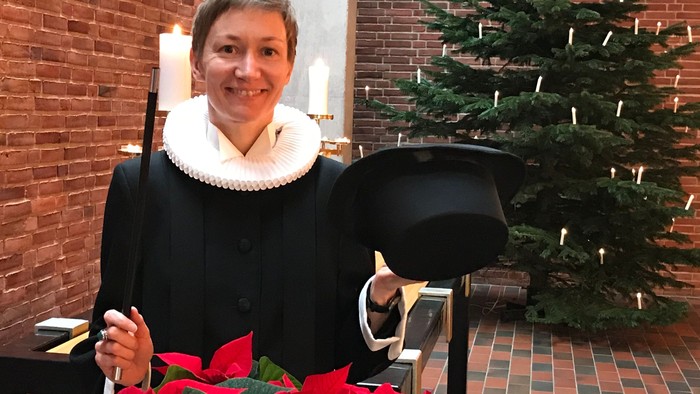 Kvinde i svart kapelletøj med hvid krage står ved juletree og poinsettia
