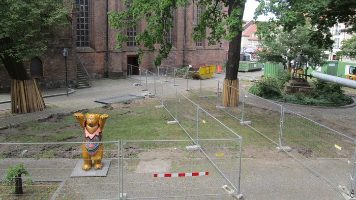 Im Bild ist eine goldene Kuhstatue vor einem Backsteingebäude mit einem Spielplatz im Vordergrund.