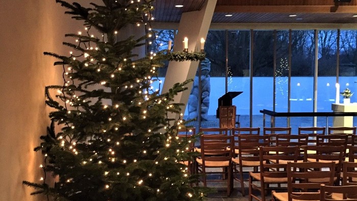 En juletree med lys og pynt i et rum med bord og stoler