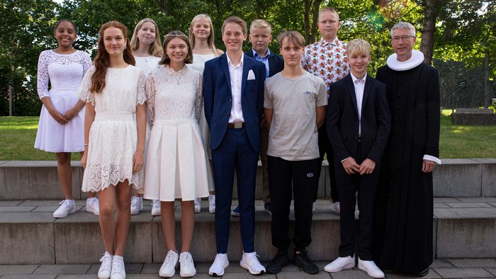 En gruppe af 13 personer står sammen på trin i en park. De er iført formelt og festligt tøj.
