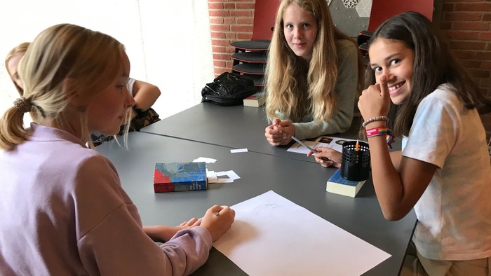 Tre unge piger sidder ved et bord og ser glade ud.