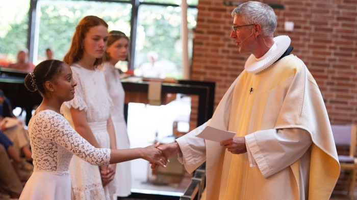En præst giver kommunion til tre unge piger i kirke.