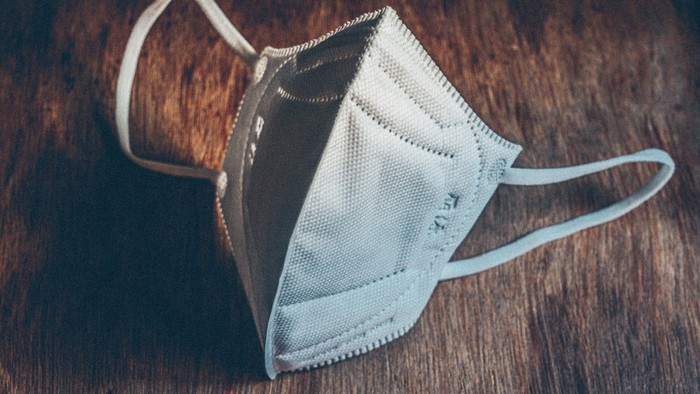 Eine graue Schutzmaske liegt auf einem Holztisch.