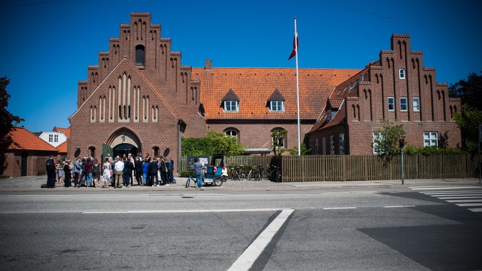 En gruppe af mennesker står foran et stort, rødt murstensbygning med spisse tårne.