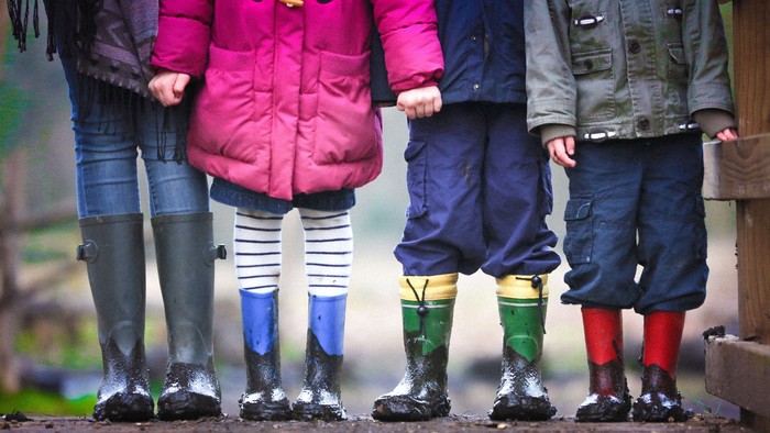 Vier Kinder in Gummistiefeln stehen im Matsch.