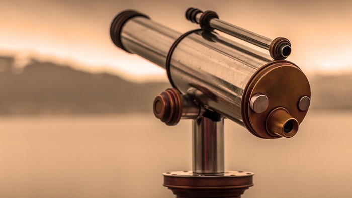 Ein Fernrohr mit zwei Okularen vor einem Bergsee bei Sonnenuntergang
